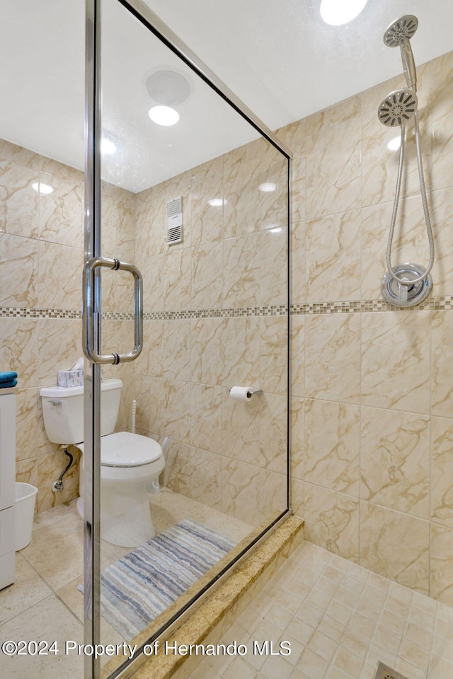 bathroom with tile walls, toilet, tiled shower, and tile patterned floors