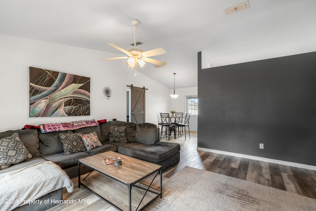 living room featuring hardwood / wood-style flooring, lofted ceiling, a barn door, and ceiling fan