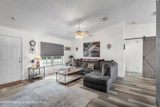 living room featuring a barn door, wood-type flooring, a textured ceiling, and ceiling fan