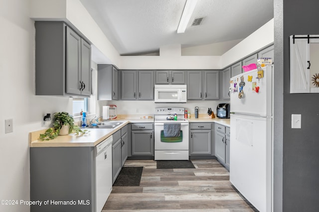 kitchen with white appliances, light hardwood / wood-style floors, vaulted ceiling, and gray cabinets