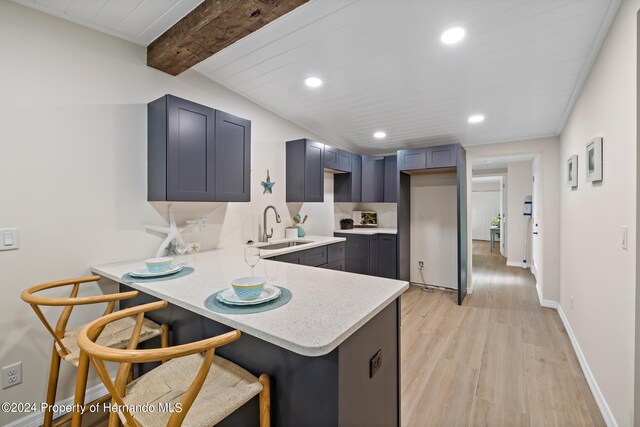 kitchen with light hardwood / wood-style floors, kitchen peninsula, sink, a breakfast bar area, and beamed ceiling