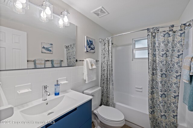 full bathroom featuring tile walls, shower / bath combination with curtain, backsplash, vanity, and toilet