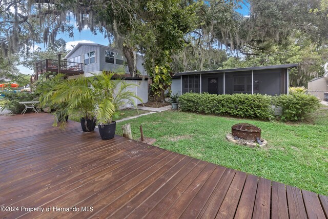 deck featuring a lawn, a sunroom, an outdoor fire pit, and a water view