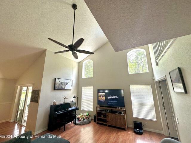 living room featuring ceiling fan, high vaulted ceiling, light hardwood / wood-style floors, and a textured ceiling