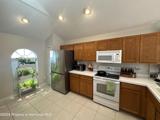 kitchen featuring vaulted ceiling, stainless steel appliances, a textured ceiling, and light tile patterned flooring