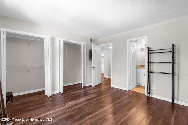 unfurnished bedroom with two closets, ensuite bath, a textured ceiling, and dark hardwood / wood-style flooring