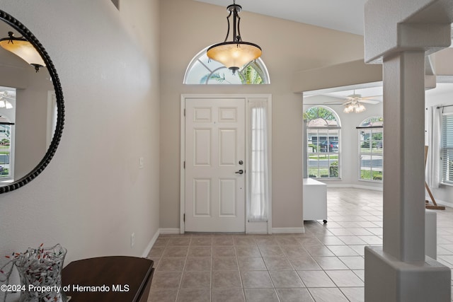 tiled foyer entrance with high vaulted ceiling, a wealth of natural light, ceiling fan, and decorative columns