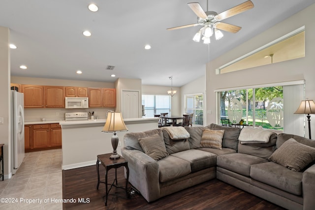 living room with a wealth of natural light, ceiling fan with notable chandelier, light hardwood / wood-style floors, and vaulted ceiling