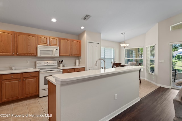 kitchen with light hardwood / wood-style floors, a center island with sink, hanging light fixtures, white appliances, and a chandelier