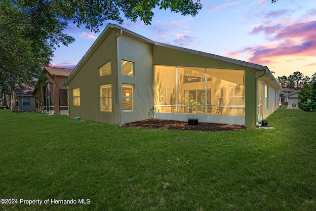 property exterior at dusk featuring a lawn and a sunroom