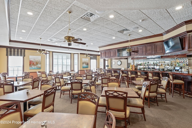 carpeted dining space featuring a healthy amount of sunlight, bar, ornamental molding, and ceiling fan