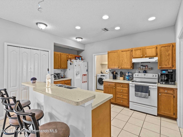 kitchen featuring sink, a kitchen breakfast bar, light tile patterned floors, white appliances, and washer / dryer