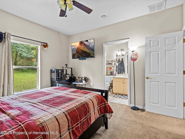 bedroom with ceiling fan, ensuite bathroom, light colored carpet, and a textured ceiling