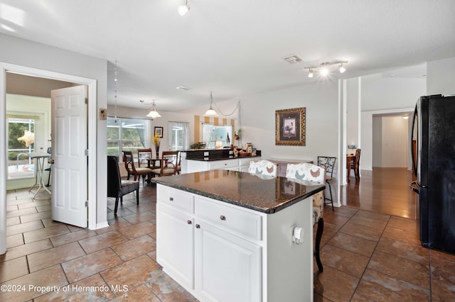 kitchen with a kitchen breakfast bar, decorative light fixtures, a center island, white cabinets, and black refrigerator