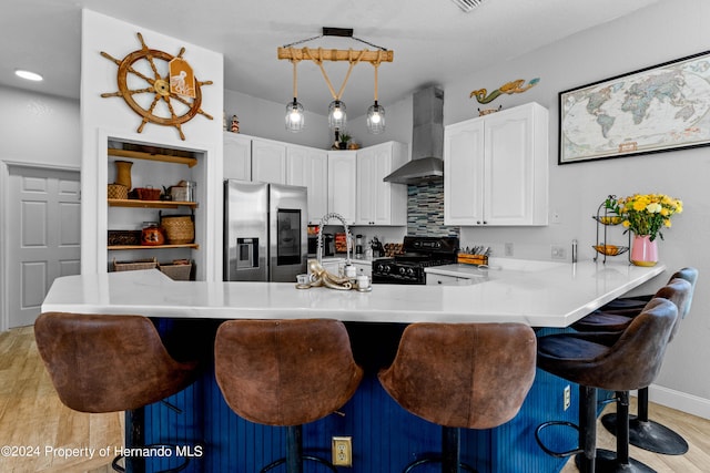 kitchen featuring a kitchen breakfast bar, stainless steel refrigerator with ice dispenser, wall chimney exhaust hood, black gas range, and light wood-type flooring