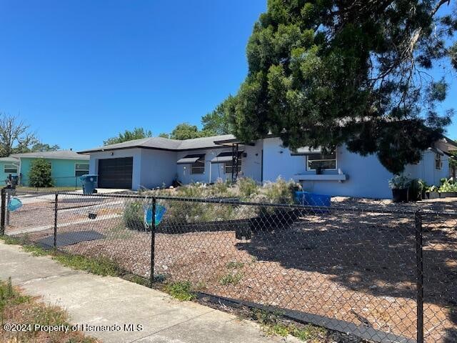 ranch-style home featuring a fenced front yard, an attached garage, and stucco siding