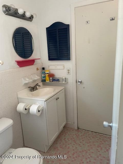 bathroom featuring vanity, tile walls, and toilet