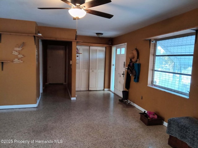 foyer entrance with a ceiling fan, speckled floor, and baseboards
