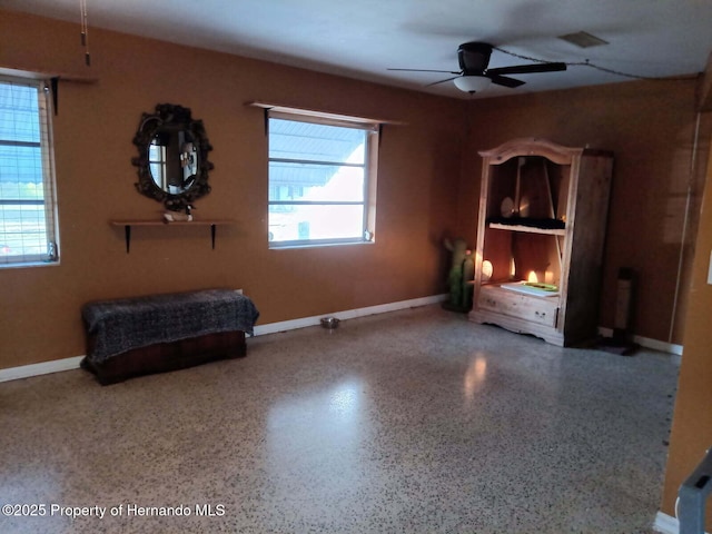 interior space with baseboards, ceiling fan, and speckled floor
