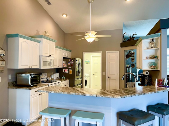 kitchen with a kitchen bar, white cabinets, kitchen peninsula, white appliances, and washer / dryer