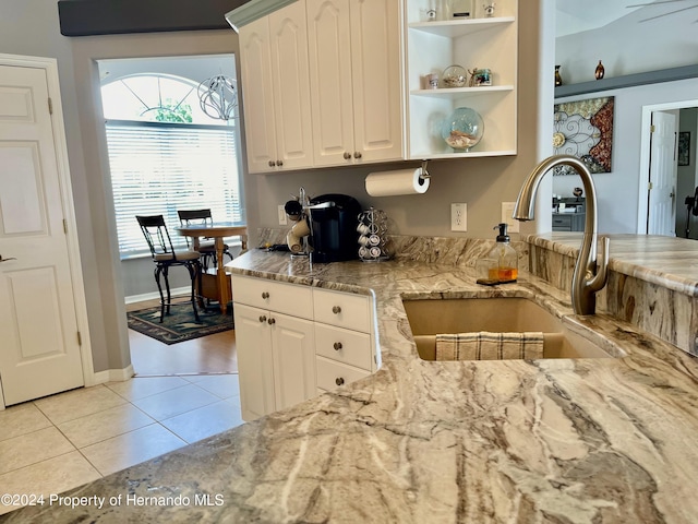 kitchen featuring white cabinets, light stone counters, light tile patterned floors, and sink