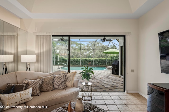 living room with light tile patterned flooring, ceiling fan, and a tray ceiling