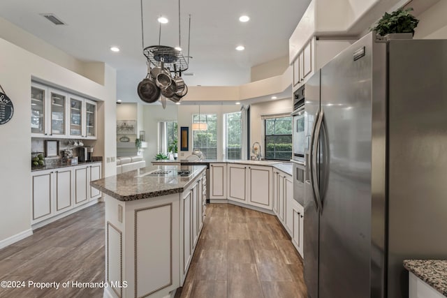 kitchen featuring light wood-type flooring, a kitchen island, stainless steel refrigerator, and dark stone countertops