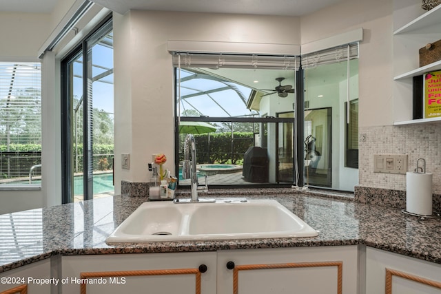 kitchen with dark stone counters, backsplash, sink, white cabinets, and ceiling fan