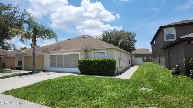 view of side of home with an attached garage, a shingled roof, concrete driveway, a lawn, and stucco siding