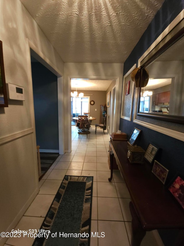 corridor with an inviting chandelier, a textured ceiling, and light tile patterned floors