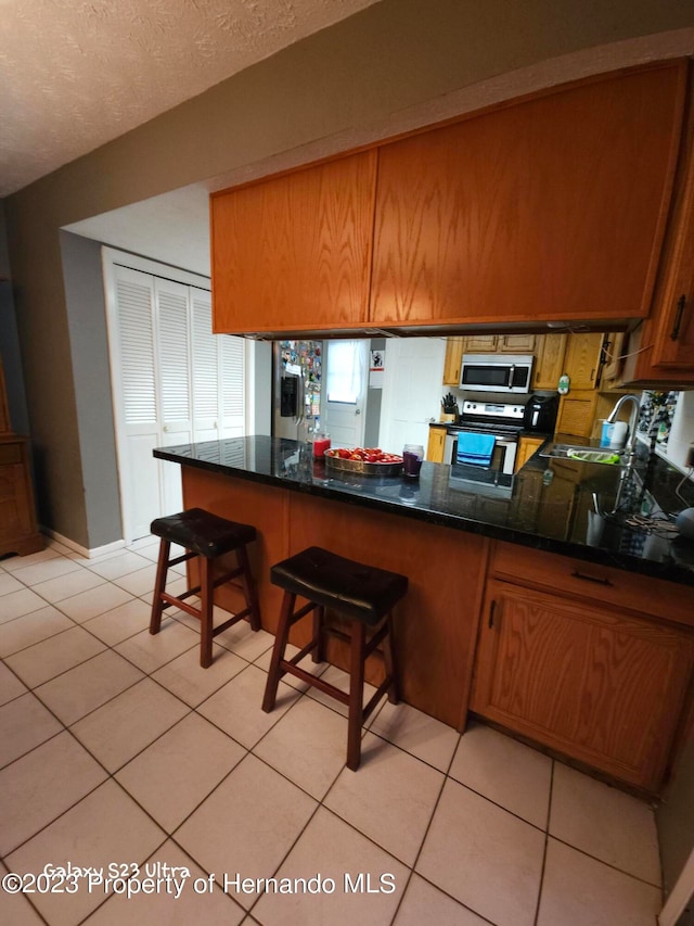 kitchen with white electric stove, kitchen peninsula, light tile patterned floors, and a breakfast bar area