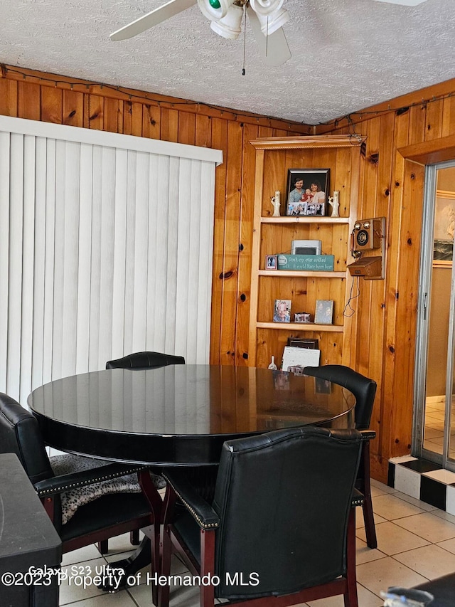 dining room featuring wooden walls, a textured ceiling, ceiling fan, and light tile patterned flooring