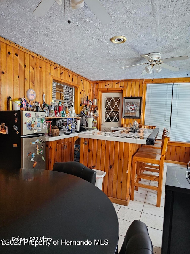 kitchen featuring kitchen peninsula, wood walls, a textured ceiling, light tile patterned flooring, and stainless steel refrigerator