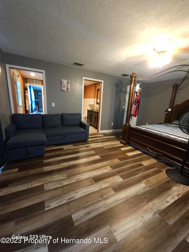 bedroom with hardwood / wood-style floors, a textured ceiling, and connected bathroom