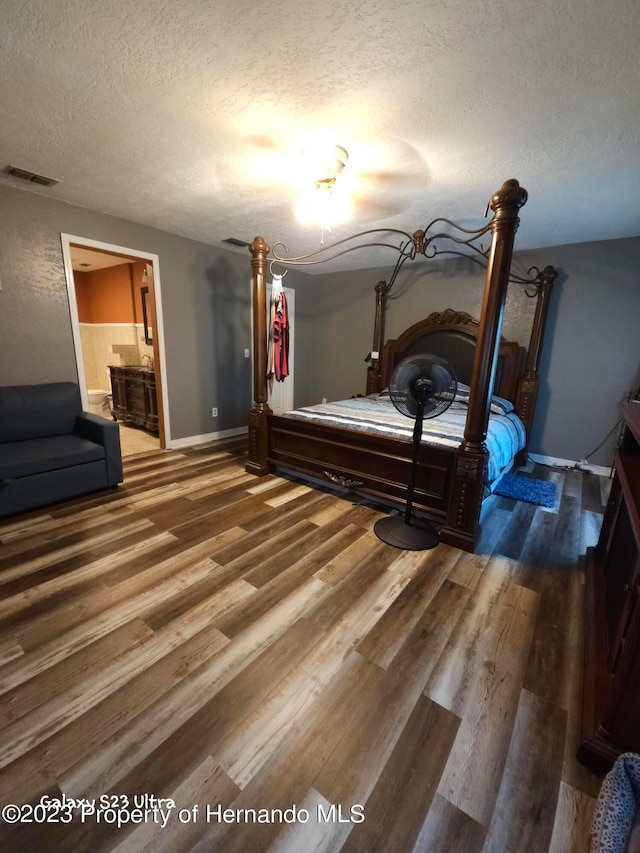 bedroom featuring ensuite bathroom, dark wood-type flooring, and a textured ceiling