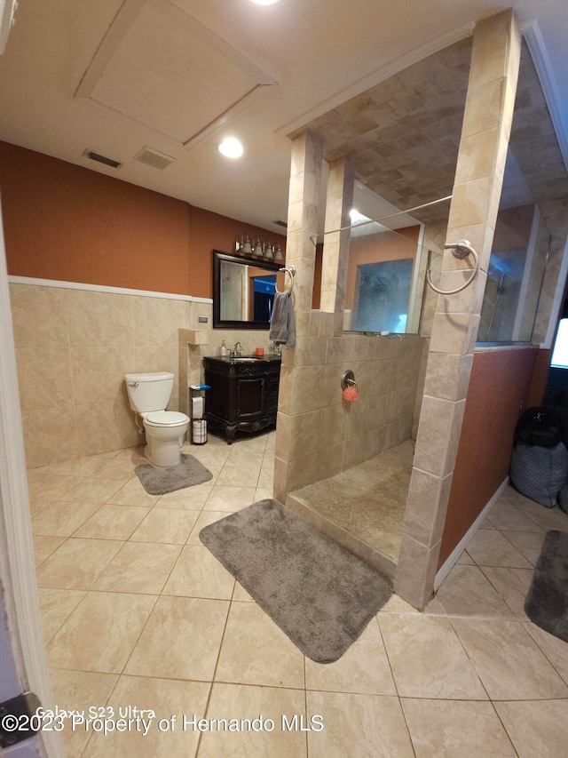 bathroom with tile patterned floors, toilet, tile walls, vanity, and a shower