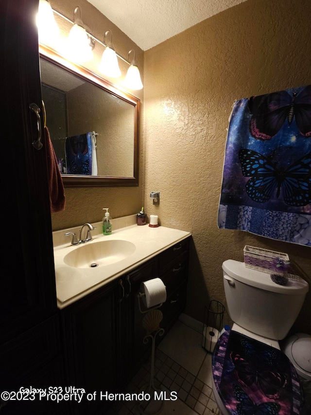 bathroom with toilet, vanity, a textured ceiling, and tile patterned floors