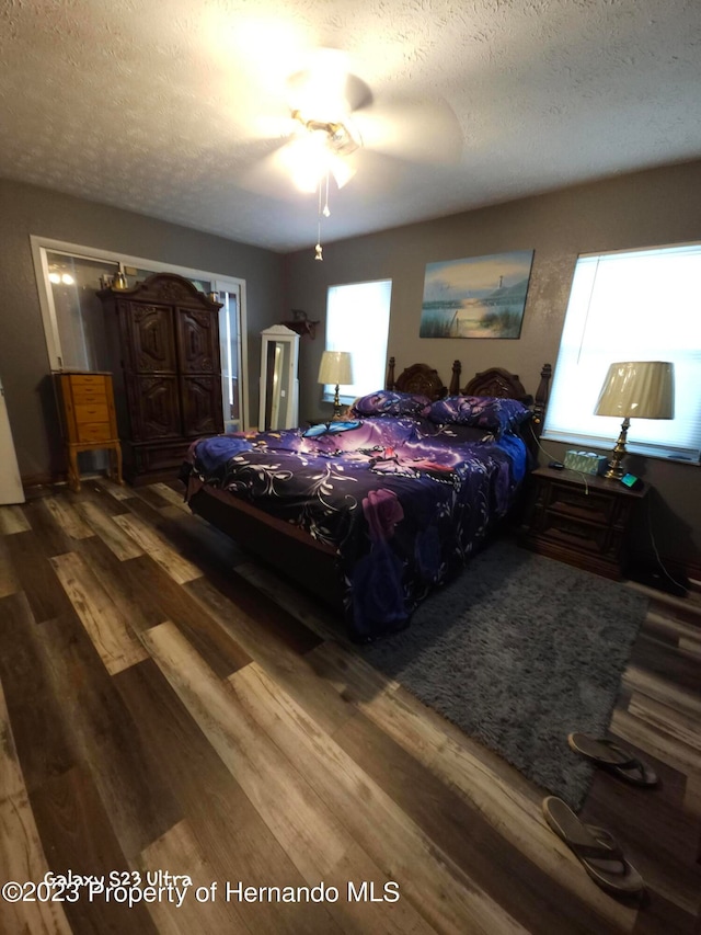 bedroom with dark hardwood / wood-style flooring, multiple windows, a textured ceiling, and ceiling fan