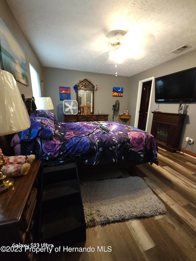 bedroom featuring a fireplace, wood-type flooring, and a textured ceiling