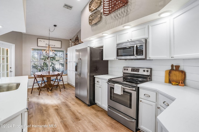 kitchen with light wood-type flooring, appliances with stainless steel finishes, white cabinets, and decorative light fixtures