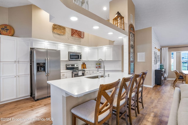 kitchen with high vaulted ceiling, a breakfast bar, sink, appliances with stainless steel finishes, and white cabinets