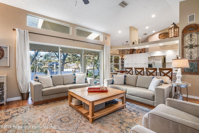 living room with ceiling fan with notable chandelier, light wood-type flooring, and high vaulted ceiling