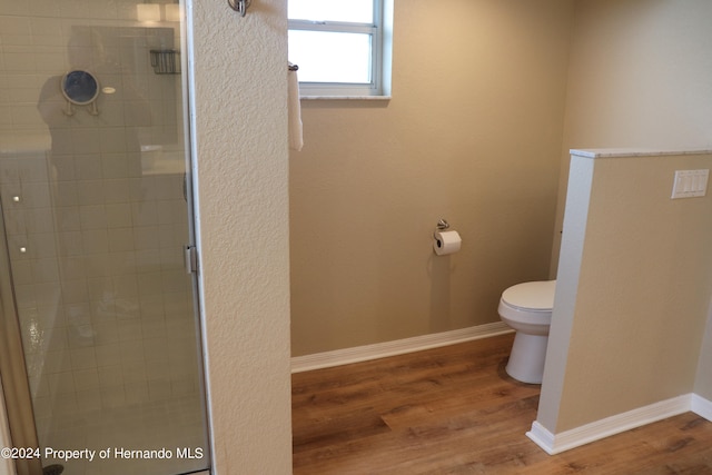 bathroom featuring hardwood / wood-style floors, a shower with shower door, and toilet