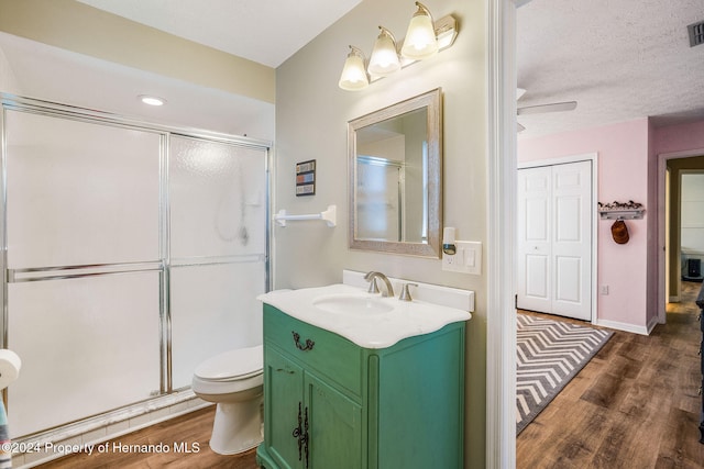 bathroom featuring toilet, a shower with door, a textured ceiling, hardwood / wood-style floors, and vanity