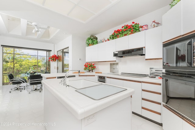 kitchen with black oven, white cabinetry, extractor fan, sink, and an island with sink