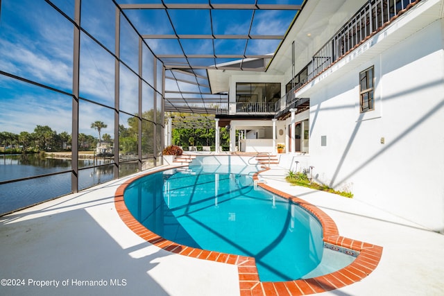 view of pool with glass enclosure, a patio area, and a water view