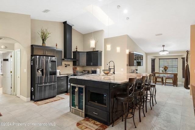 kitchen featuring wall chimney exhaust hood, light stone countertops, pendant lighting, appliances with stainless steel finishes, and wine cooler