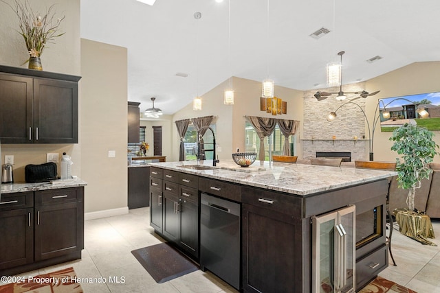 kitchen featuring sink, a kitchen island with sink, dark brown cabinets, a fireplace, and decorative light fixtures