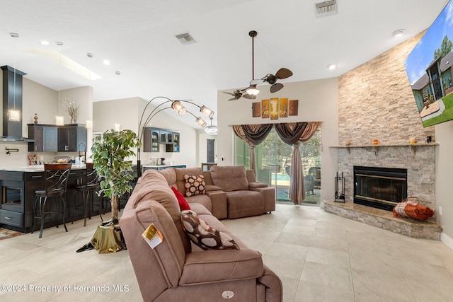 living room with a high ceiling, ceiling fan, light tile patterned floors, a skylight, and a stone fireplace