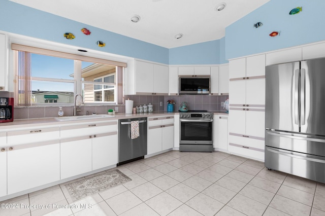 kitchen with appliances with stainless steel finishes, decorative backsplash, sink, vaulted ceiling, and white cabinets